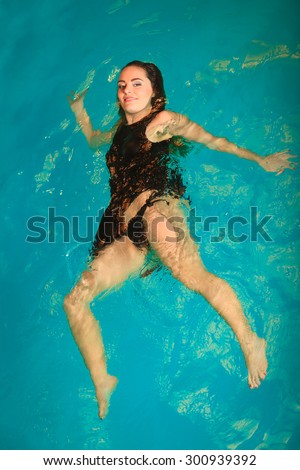 Woman relaxing at swimming pool. Young girl wearing black dress floating. Water aerobics fitness.