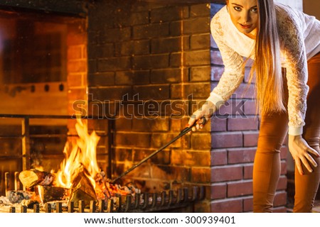 Woman with fire iron poker at fireplace. Young girl heating warming up and relaxing. Winter at home.