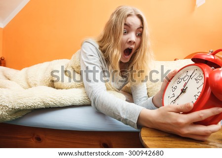 Panic woman waking up late in morning turning off alarm clock. Young girl laying in bed.