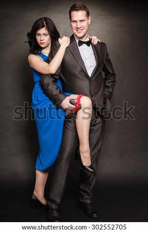 Women men relationship. Woman in blue dress and man with gun in suit on black background.