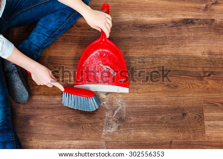 Cleanup housework concept. Closeup cleaning woman sweeping wooden floor with red small whisk broom and dustpan indoor