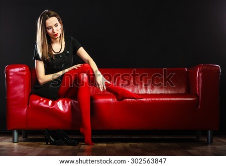 Elegance and fashion outfit. Fashionable woman legs in red vivid color tights posing on couch black background
