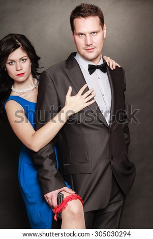 Women men relationship. Woman in blue dress and man with gun in suit on black background.