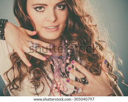 Pretty young woman wearing many plenty of jewelry necklaces beads, rings and bracelets. Portrait of gorgeous fashion girl in studio on blue.