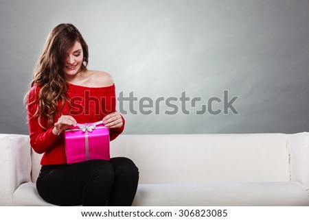 People celebrating xmas love and happiness concept - beauty girl opening present pink gift box sitting on sofa at home