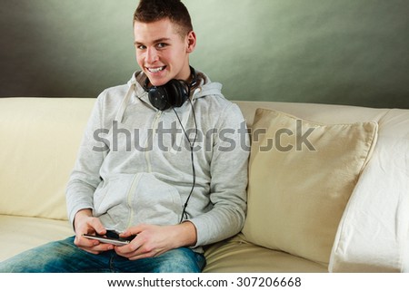 Modern technologies connection leisure concept. Young handsome man relaxing on couch with headphones smartphone at home