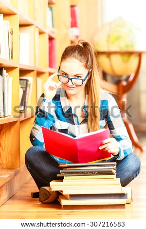 Education school concept. Clever female student hair ponytail girl blue glasses sitting on floor in college library with stack books. Indoor