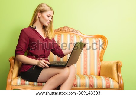 Young fashionable woman girl sitting on vintage retro sofa couch using laptop computer surfing the internet. Fashion and modern technology.