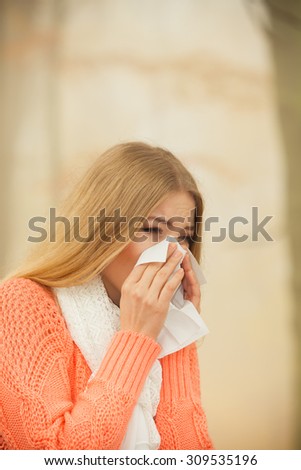 Sick woman in fall autumn park sneezing in tissue. Ill girl caught cold flu outdoor. Rhinitis or allergy. Health care.
