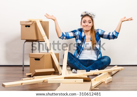 Funny woman moving into new apartment house assembling furniture. Young girl screws and parts on head arranging interior and unpacking boxes.