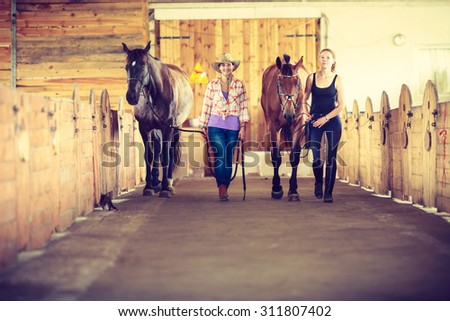 Western cowgirl and young woman walking with horses in stable paddock. Instagram filter.