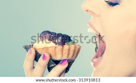 Sweet food indulging and fattening concept. Woman face profile wide open mouth eating cake cupcake filtered photo