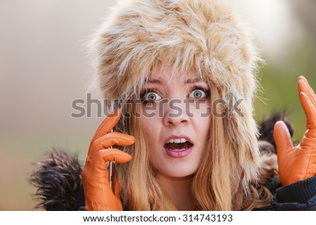 Portrait of scared afraid pretty woman talking on mobile phone. Gorgeous young girl in fur winter hat and jacket. Autumn fashion and communication.