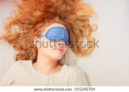 Tired woman sleeping in bed wearing blindfold sleep mask. Young girl taking nap.