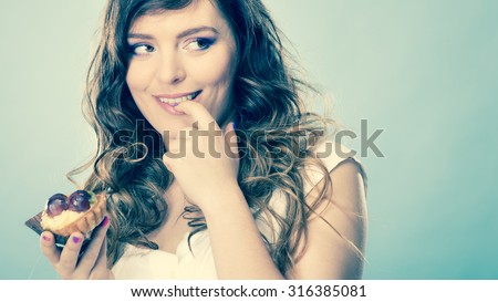 Bakery, sweet food and people concept. Closeup smiling cute woman curly hair holding fruit cake cupcake in hand on blue
