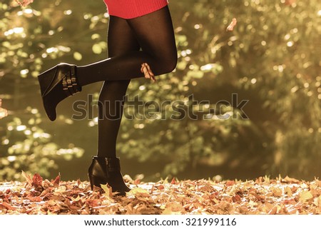 Autumn fashion. Female legs in black pantyhose and stylish fashionable shoes boots, outdoor golden leaves