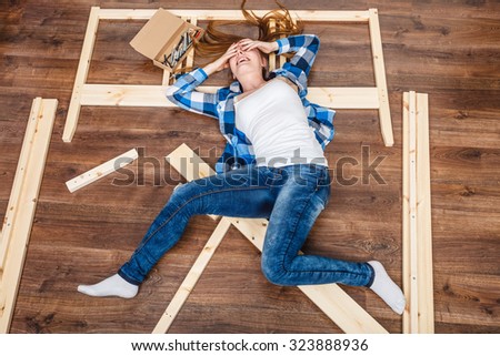 Happy woman having fun assembling furniture at home. Young girl laying on floor arranging apartment house interior. DIY. High angle view.