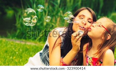 Mother and little girl daughter child blowing soap bubbles outdoor. Parent and kid having fun in park. Happy and carefree childhood. Good family relations.