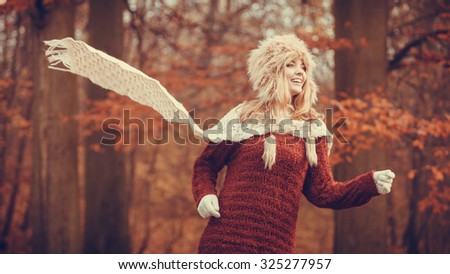 Fashion woman with flying scarf running in fall autumn park forest against blowing wind. Young girl in fur cap and sweater having fun outdoor.