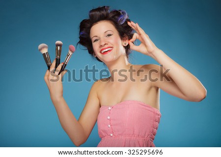 Cosmetic beauty procedures and makeover concept. Woman in hair rollers holding makeup brushes set making ok sign gesture on blue