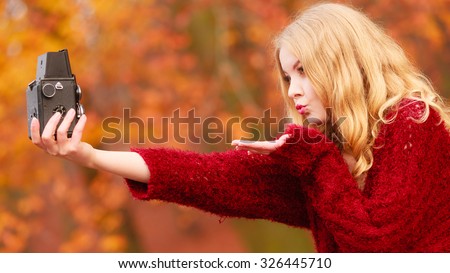 Pretty woman in fall forest park taking selfie self photo with old vintage camera. Gorgeous young girl passionate photographer blowing kiss. Autumn winter photography.