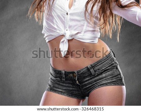 Closeup of sexy alluring woman hips and belly. Slim girl wearing white shirt and jeans shorts. Hotness and sexiness.