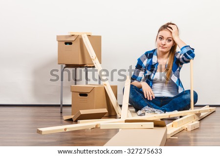 Worried woman moving into new apartment house assembling furniture. Young girl arranging interior and unpacking boxes.