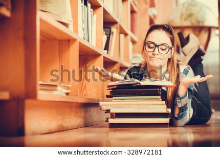 Education school concept. Clever female student girl in glasses lying on floor in college library with stack books reading. Indoor