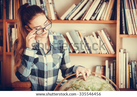Education travel and geography concept. Hipster lovely woman female student in blue glasses in library with globe. Instagram filter