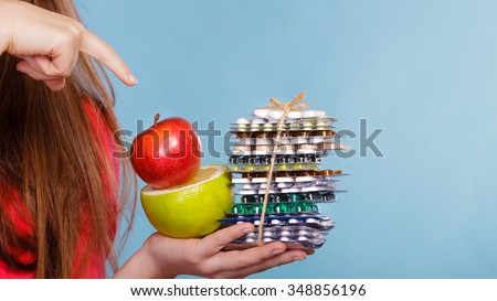 Closeup of human hands holding vitamin tablets pills and fruits. Choice between natural and synthetic vitamins. Health care. Healthy lifestyle nutrition concept.