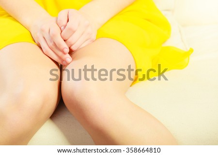 Closeup young woman sitting on couch, only the legs and the lap is showing, she is shy