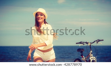 Sport and recreation. Young girl in straw hat resting after cycling on beach. Smiling tourist spending time on seaside. Leisure in summer.
