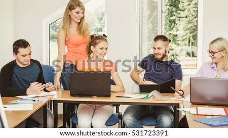 Teaching helping technology concept. Woman young teacher or tutor with adult students in classroom at desk with papers, laptop computer. Studies course