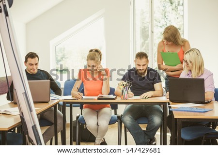 Teaching Concept. Female young teacher or tutor with adult students in classroom with papers, laptop computer. Studies course