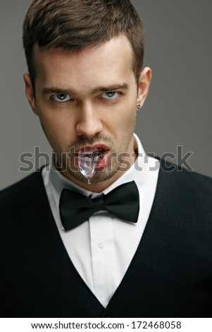 young man man in a black suit with a white shirt and a butterfly in the studio with ice in mouth