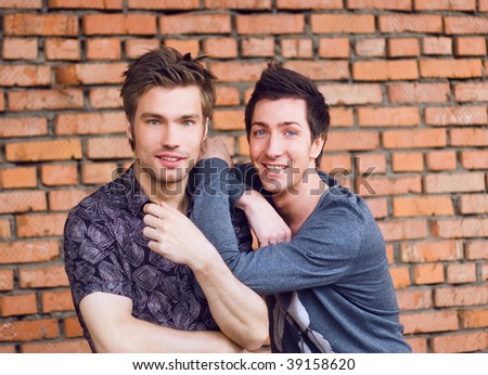 two smiling youth Friends embracing   at the brick wall
