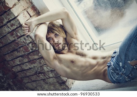 bearded handsome man sitting on a sill at the window with brick wall and his hands up