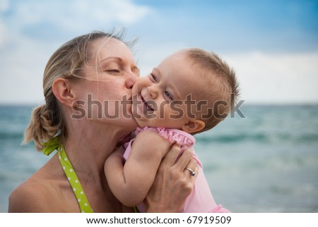 New mom kisses happy baby on a sunny day at the beach