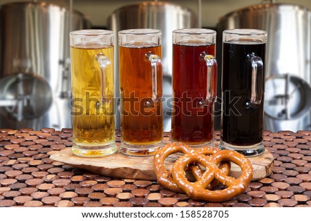 beer flight of four sampling mugs of light and dark craft beer with beer fermenter background