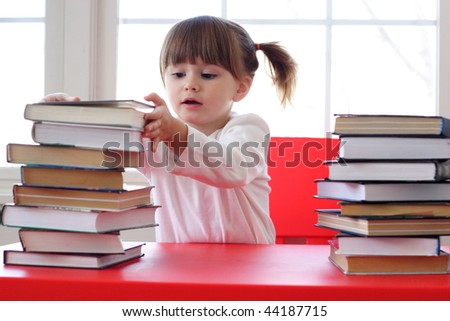 Toddler girl with pile of books on the table