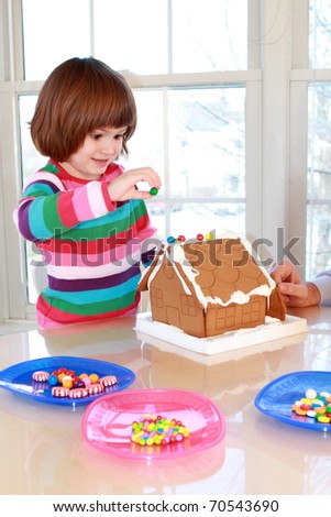 Little girl decorating gingerbread house with colorful candy for Christmas