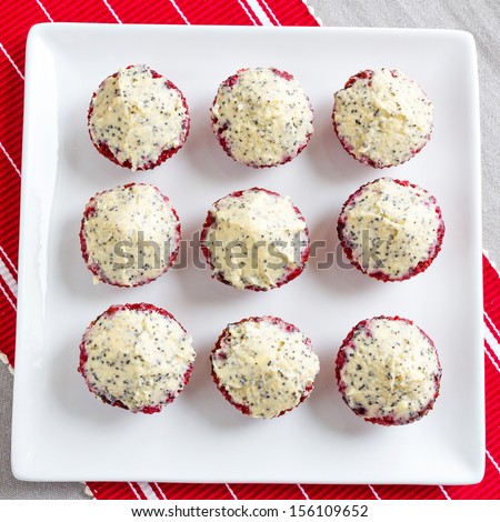 Delicious, mini sized, gluten free, red beetroot cupcakes. Butter and cream cheese topping with vanilla and poppy seeds. creative and colorful. Placed on a red table runner.