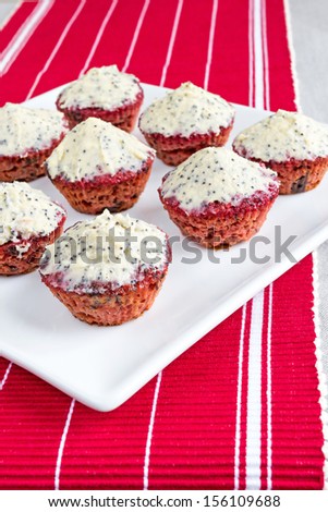 Delicious, mini sized, gluten free, red beetroot cupcakes. Butter and cream cheese topping with vanilla and poppy seeds. creative and colorful. Placed on a red table runner.