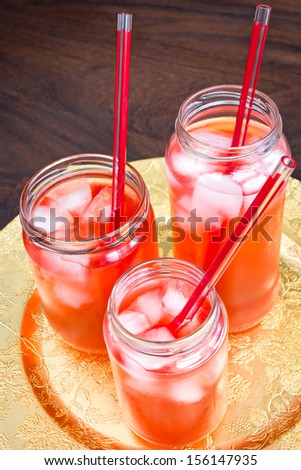 Three mason jars in different sizes and shapes with ice, drinks and a straw. This is home made ice tea, but could just as well be lemonade.