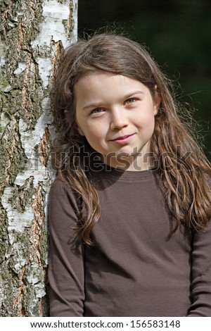 Dark haired cute girl leaning against a birch tree in the sun