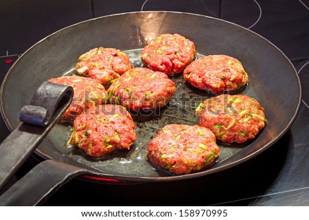 Cooking flat meatballs with zucchini mixed in, in a beautiful forged iron pan. A healthy meal.