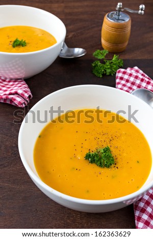 Colorful creamy soup made of pumpkin, sweet potato and coconut milk. Decorated with parsley and fresh ground black pepper. Two servings