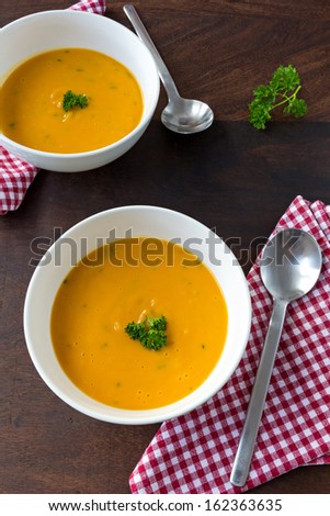Colorful creamy soup made of pumpkin, sweet potato and coconut milk. Decorated with parsley. Two servings