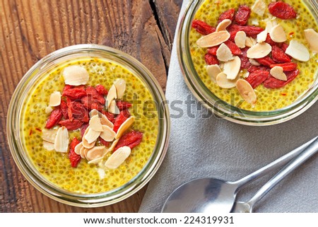 Healthy homemade yellow chia seed puddings with saffron topped with goji berries and almonds and served in glass jars