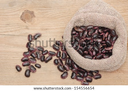 Burlap sack with purple beans on a wooden background